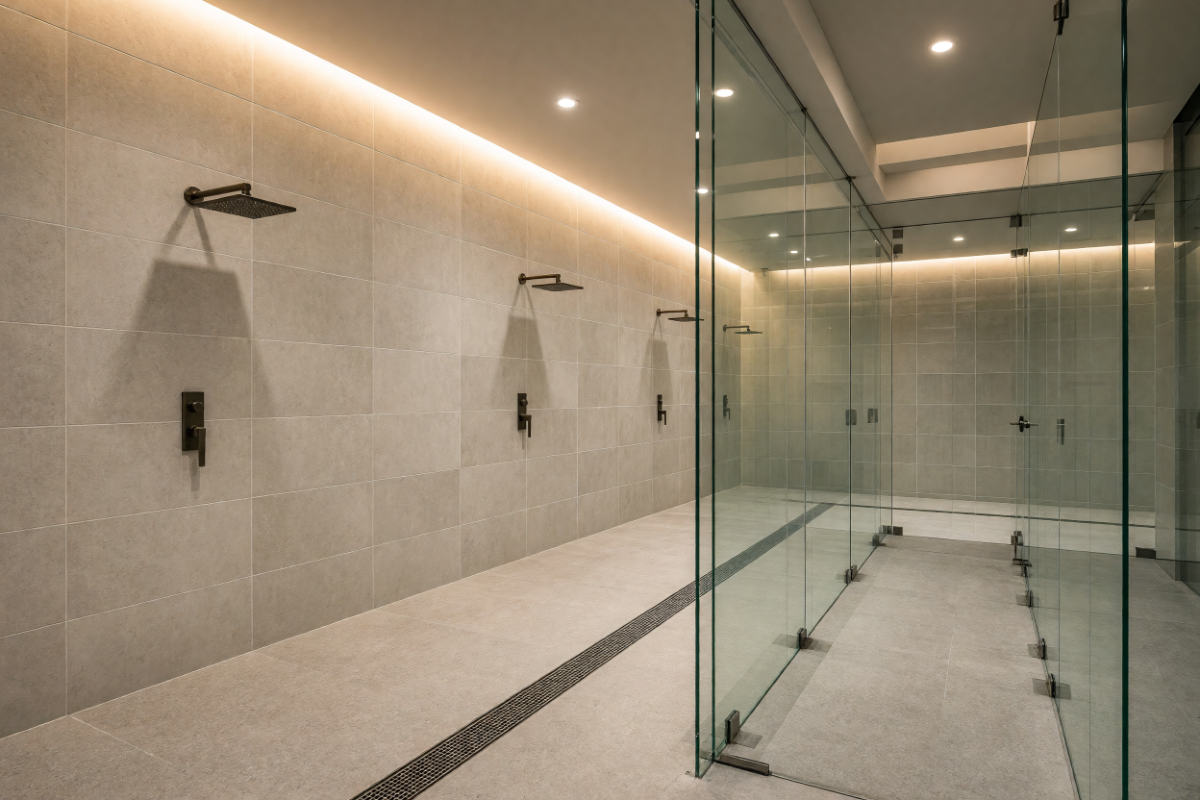 Locker room shower with large porcelain wall tile, linear drain and glass partitions